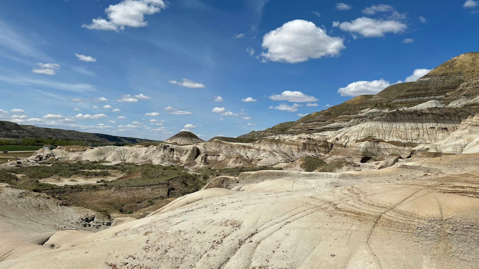 Pale badlands slopes in the Drumheller valley under a blue sky with scattered white clouds