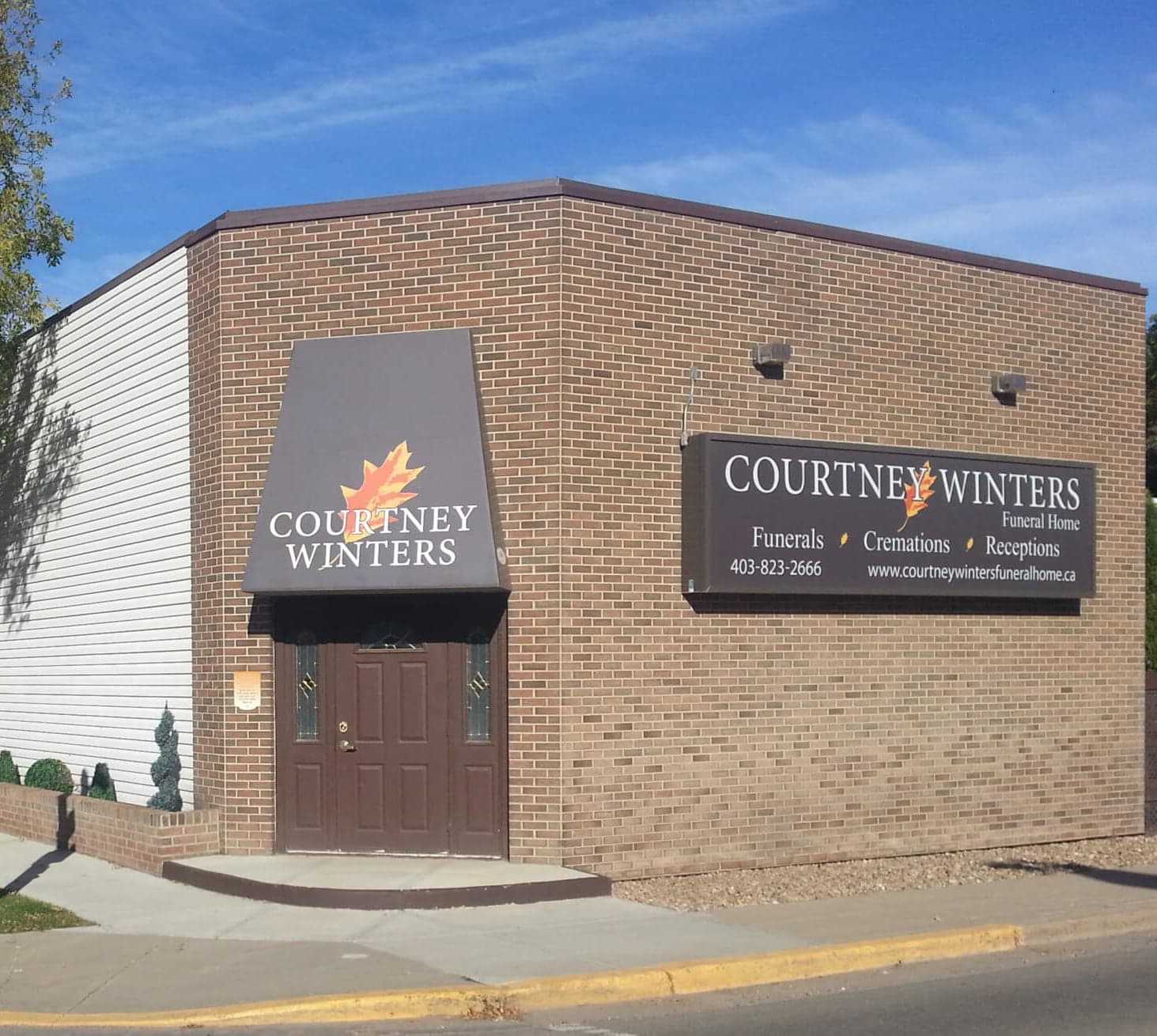 The front entrance of Courtney-Winters Funeral Home in Drumheller: a brown door beneath a maple-leaf awning, beside the sign reading Funerals, Cremations, Receptions